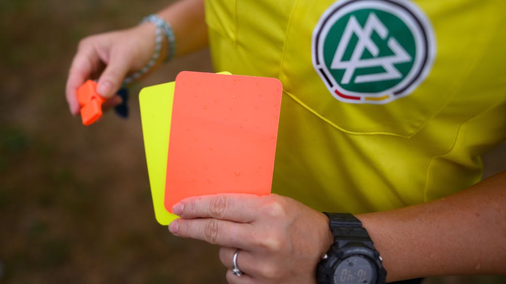 Eine Schiedsrichterin zeigt eine Rote und eine Gelbe Karte.
