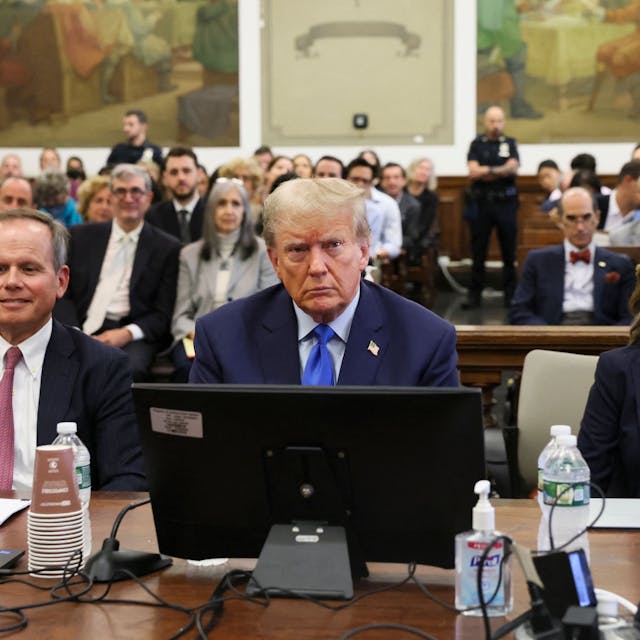Donald Trump sitzt in einem Gerichtssaal hinter einem Bildschirm, neben ihm sitzen seine Anwälte.