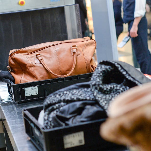 Ein Sicherheitsmitarbeiter kontrolliert Handgepäck an einem Flughafen. Die Maße und Gewicht für Handgepäck will das EU-Parlament künftig vereinheitlichen, um Reisende vor versteckten Kosten zu schützen.