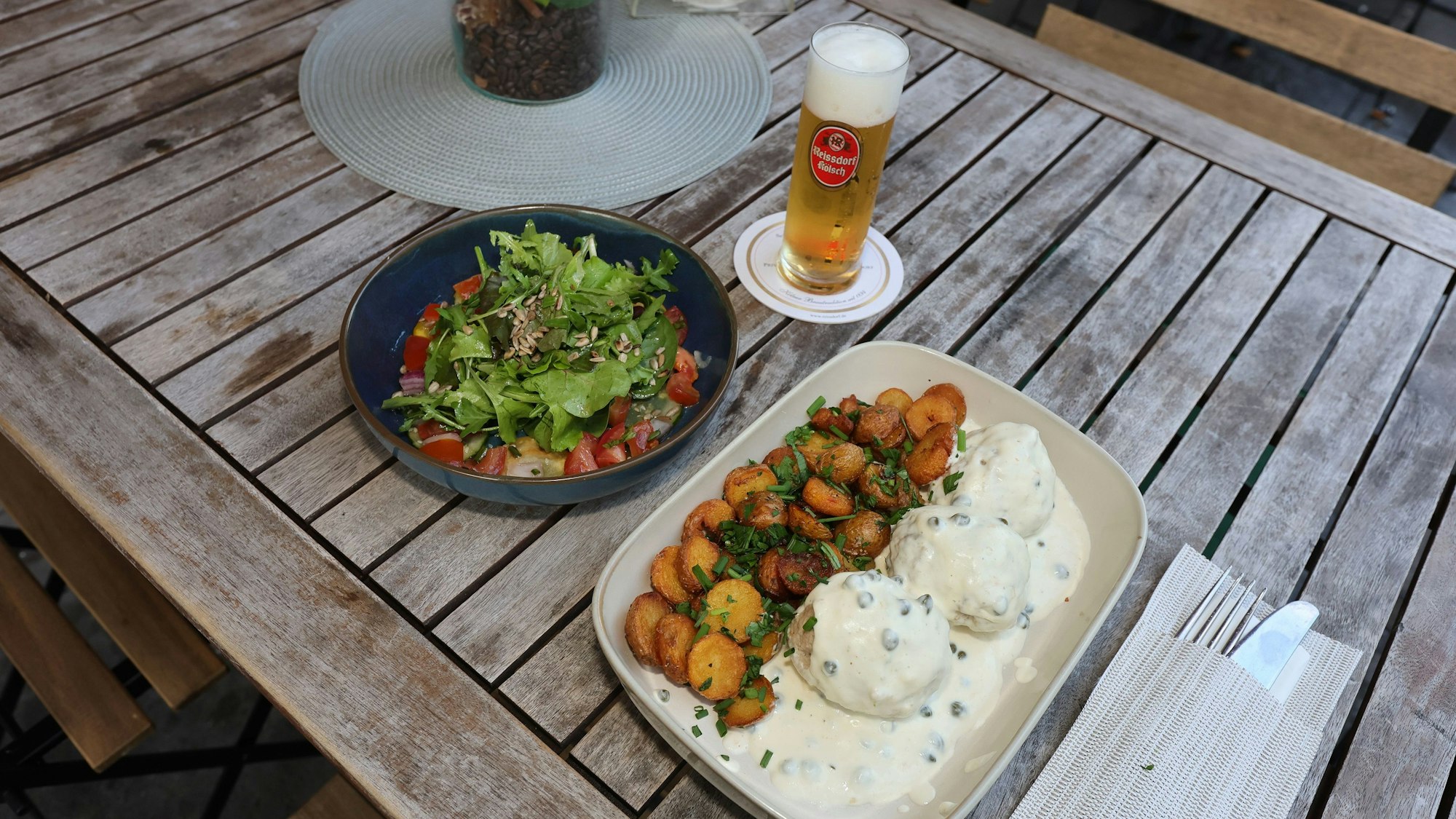 Königsberger Klopse mit Salat und einem Kölsch auf einem Holztisch
