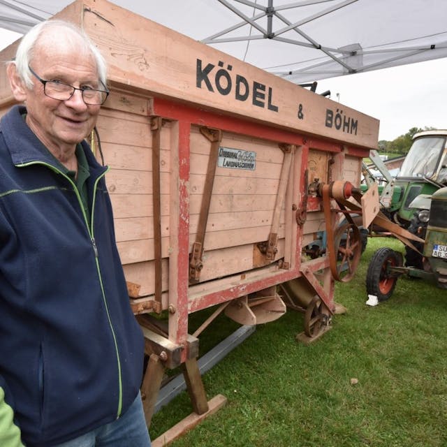 Der Mitgründer der Deutz-Schlepper-Freunde, Manfred Keuenhof, steht neben einer sehr alten Dreschmaschine und einem Traktor-Oldtimer.