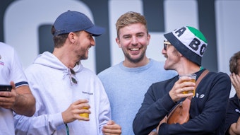 Links im Bild ist Tommi Schmitt mit einem Bier in der Hand. Neben ihm steht Christoph Kramer. Beide lachen zusammen mit einem Bekannten.