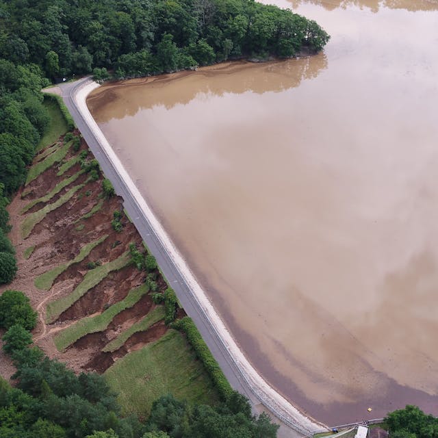 Das Bild zeigt die Steinbachtalsperre nach der Flut. Auf der Luftseite des Damms ist viel Erdreich abgerutscht.
