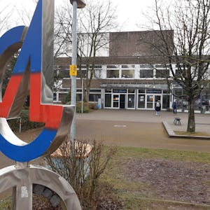 Eine Metallplastik in Blau und Rot zeigt die Buchstaben A und G vor dem Gymnasium in Siegburg