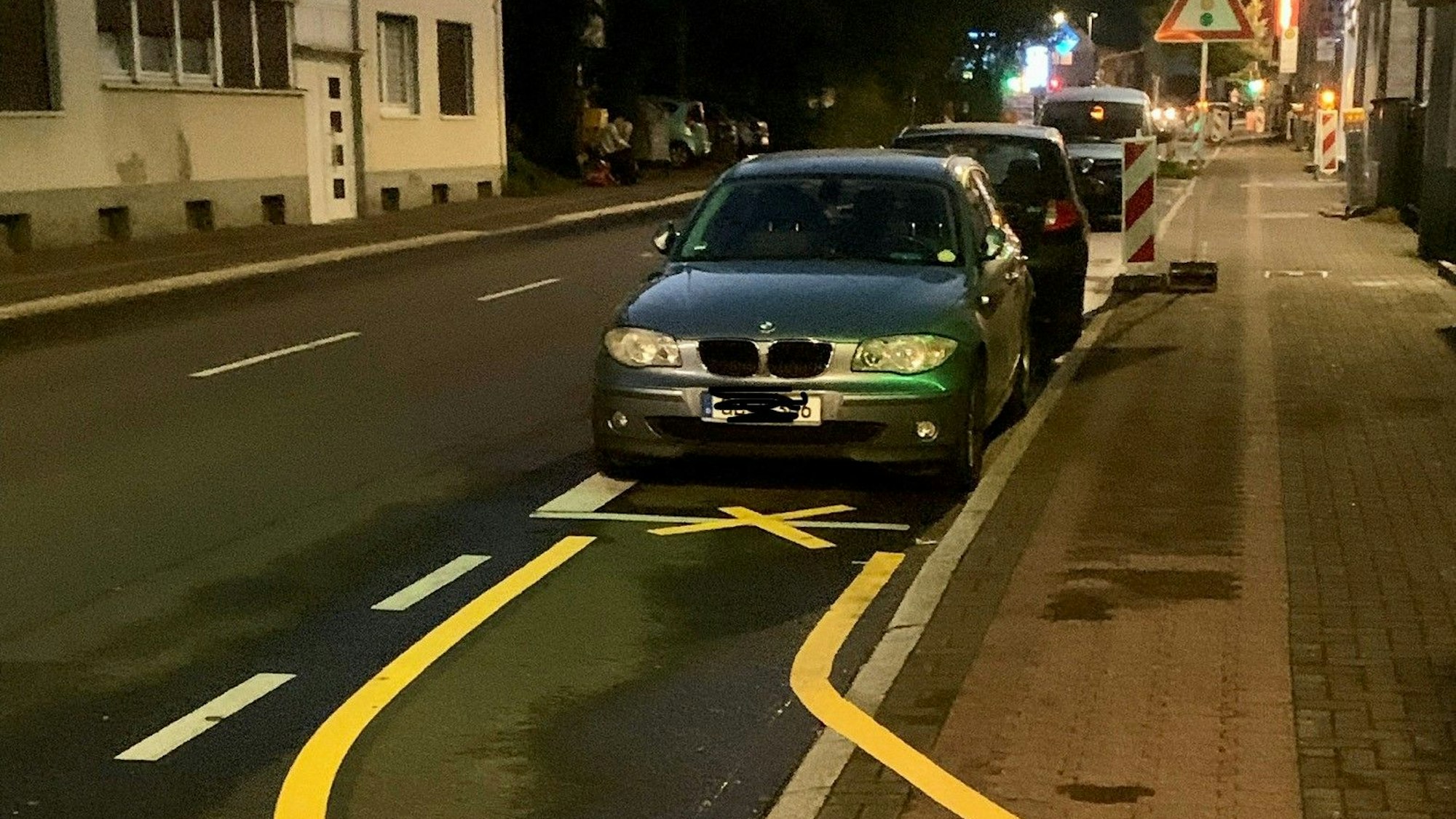 Zwei Autos parken auf dem Parkstreifen, obwohl ein gelbes X darauf hinweist, dass sie dort nicht stehen dürfen.