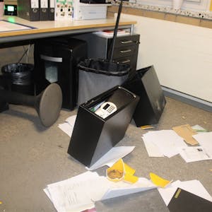 Auf dem Boden eines Büros liegt ein aufgebrochener Tresor, Papiere und zerschlagene Gegenstände.