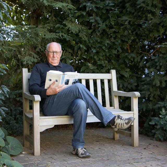 Der Autor Günther Rüther sitzt auf einer Bank im Grünen und liest.