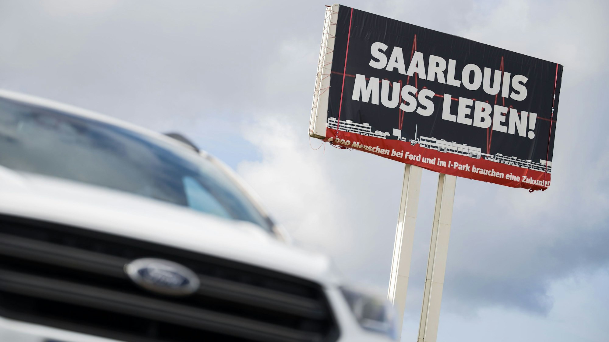 Ein Ford Kuga steht vor einem großen Schild, auf dem für die Bedeutung des Ford Werks in Saarlouis geworben wird.