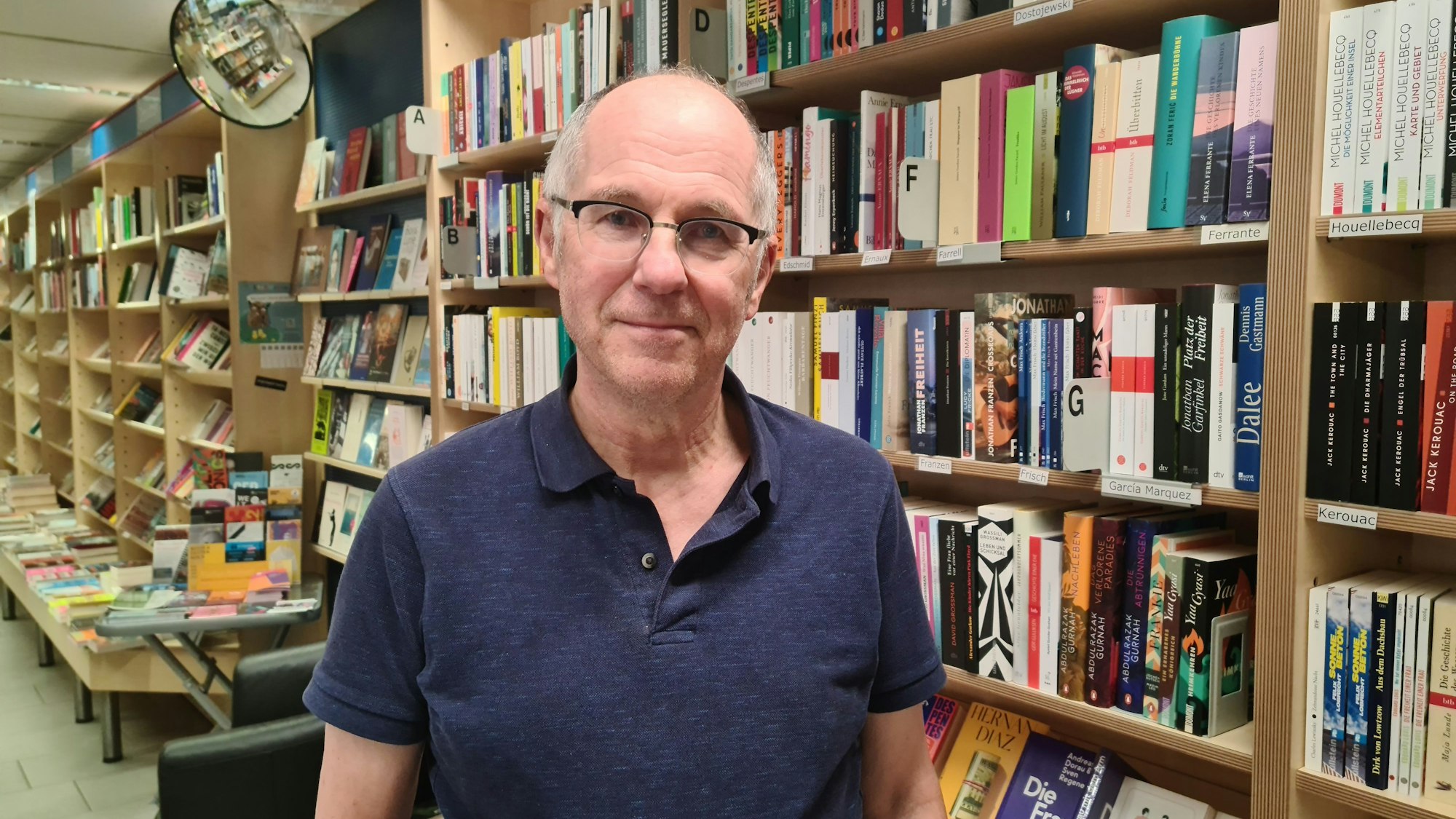 Ein Mann mit grauem Haar und Brille steht vor einem Bücherregal.