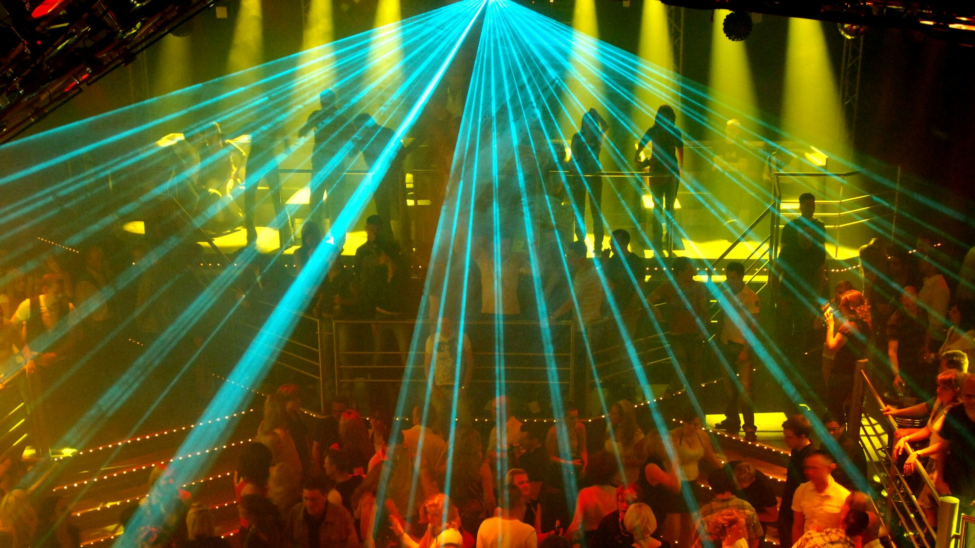 Eine Laseranlage beleuchtet eine tanzende Menschenmenge in einer Großraumdiscothek.