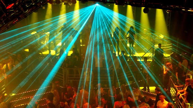Eine Laseranlage beleuchtet eine tanzende Menschenmenge in einer Großraumdiscothek.