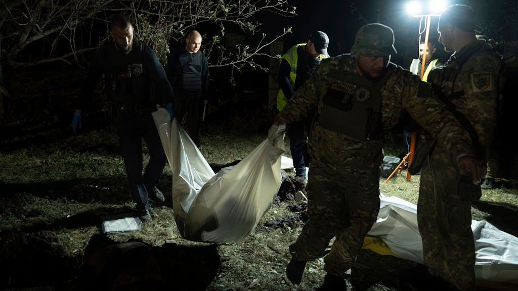 Ukrainische Polizisten tragen im Dorf Hrosa in der Nähe von Charkiw (Ukraine) die Leiche einer Person, die bei einem russischen Raketenangriff getötet wurde.