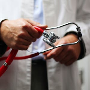 Ein Arzt in weißem Kittel hält ein Stethoskop in den Händen.