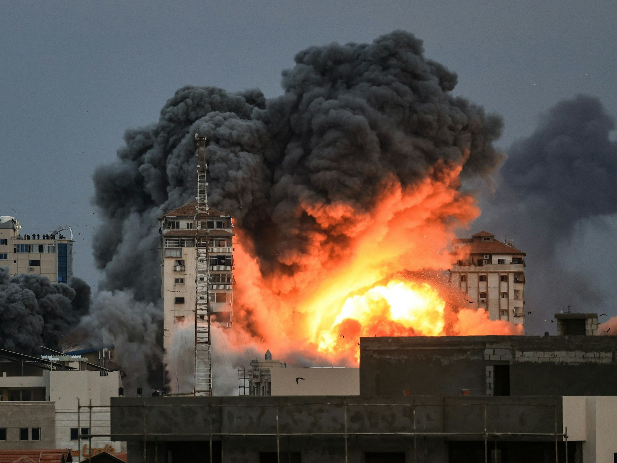 Menschen, die auf einem Dach stehen, beobachten, wie am 7. Oktober 2023 während eines israelischen Luftangriffs ein Feuer- und Rauchball über einem Gebäude in Gaza-Stadt aufsteigt.