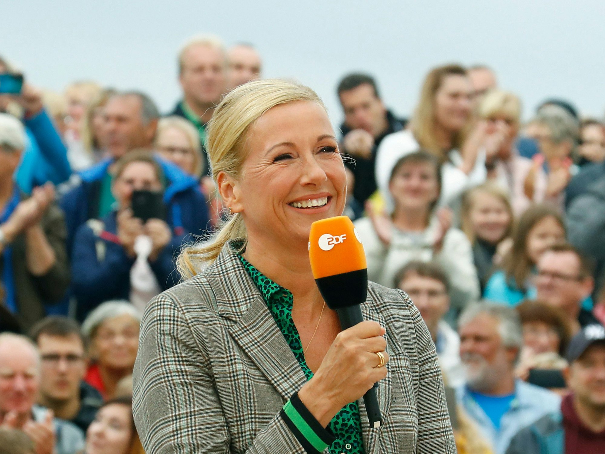 Andrea Kiewel steht im „Fernsehgarten“ und hält ein ZDF-Mikro in der Hand.