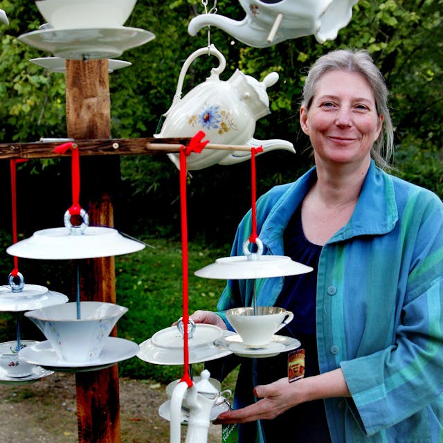 Eine Frau steht neben einer Konstruktion aus Untertassen und Teekannen.