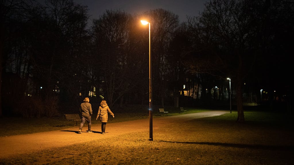 Zwei Personen gehen durch einen dunklen Park in Köln.