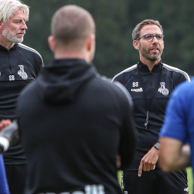 Trainer Boris Schommers spricht zu den Duisburger Fußballern, die im Halbkreis vor ihm stehen.