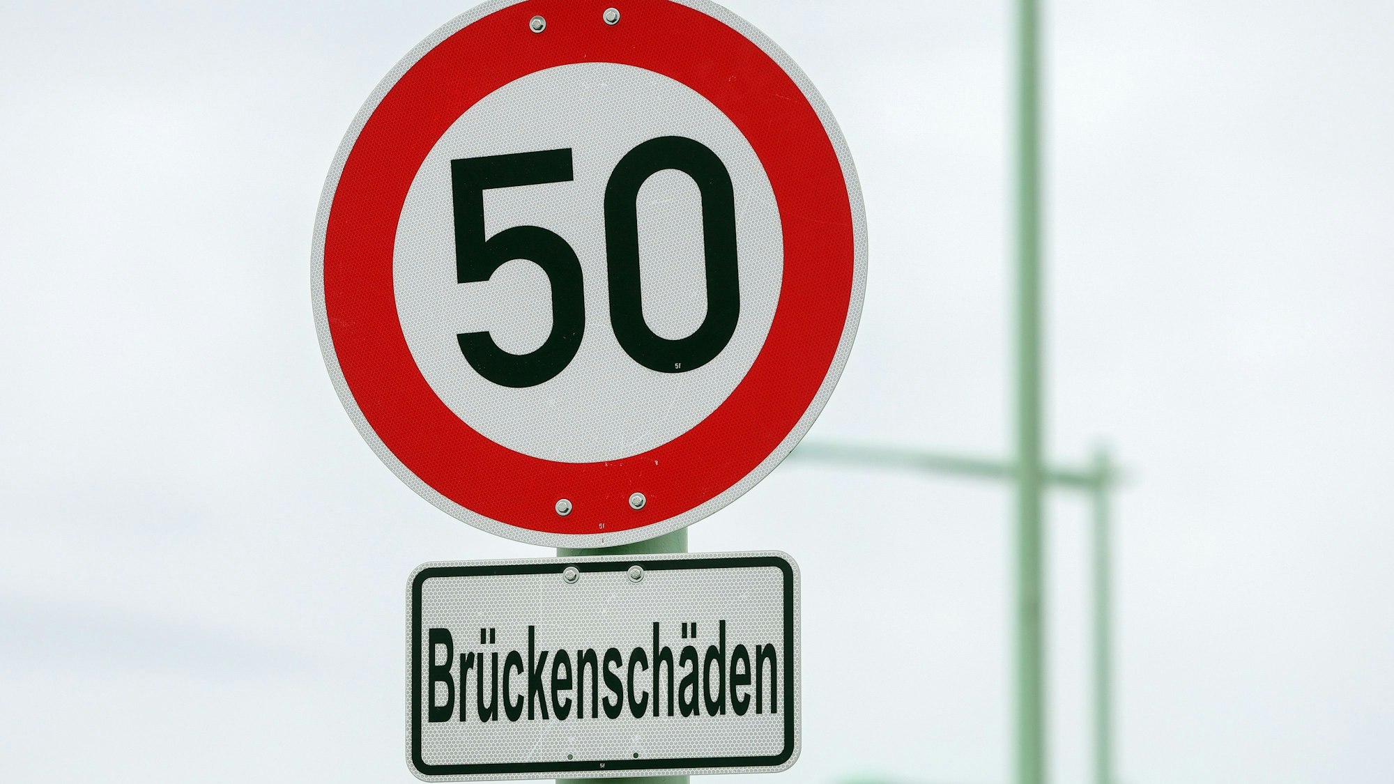 Auf einem Schild stehen 50 als zulässige Höchstgeschwindigkeit, darunter ein Hinweis auf Brückenschäden.