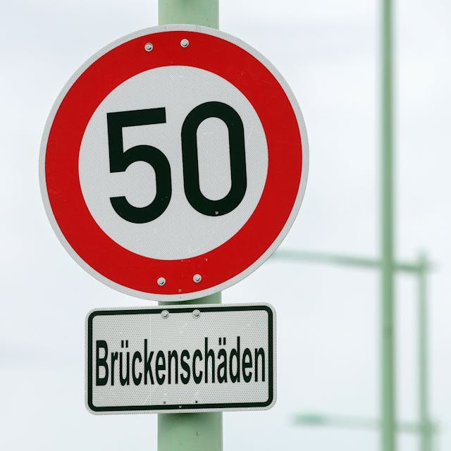 Auf einem Schild stehen 50 als zulässige Höchstgeschwindigkeit, darunter ein Hinweis auf Brückenschäden.