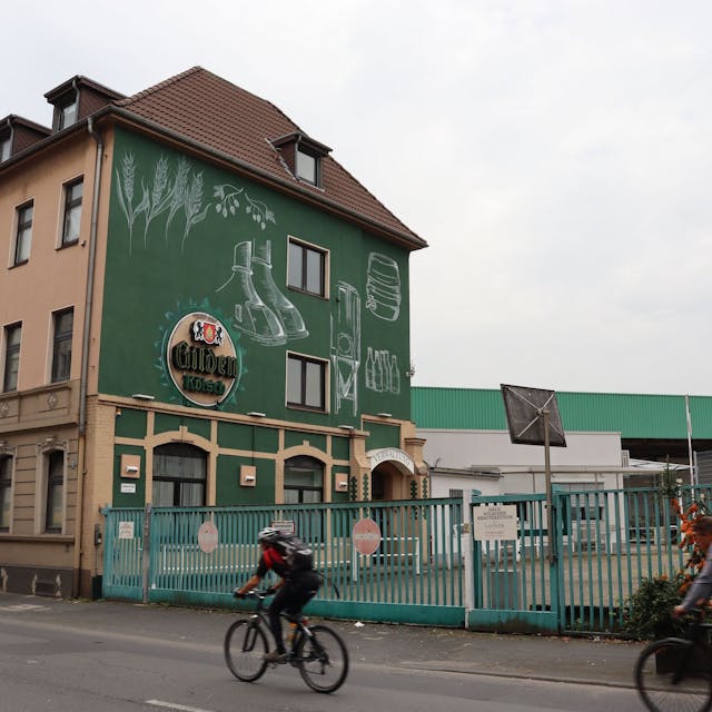 Die Gilden-Brauerei mit einer Straße und zwei Fahrradfahrer im Vordergrund.