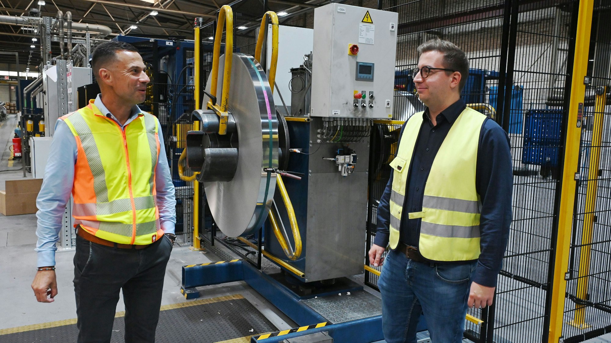 Geschäftsführer Frank Poschen (l.) und Energiemanager Marian Jansen stehen an einer Maschine in einer Produktionshalle der Firma Schoeller in Hellenthal und unterhalten sich.