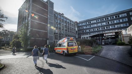 Die Notfallambulanz des Klinikums Leverkusen von außen, ein Rettungswagen steht davor, zwei Pflegerinnen sind von hinten zu sehen.