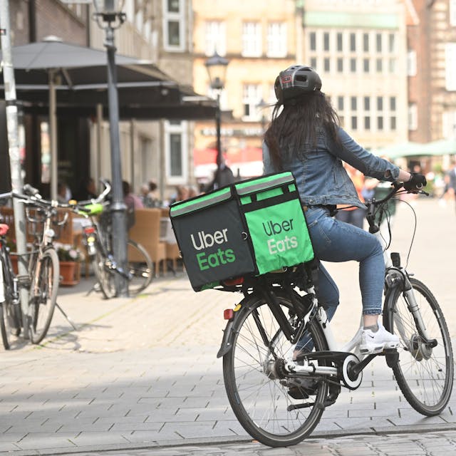Eine Lieferantin fährt auf einem Fahrrad mit Uber Eats Gepäcktasche.&nbsp;