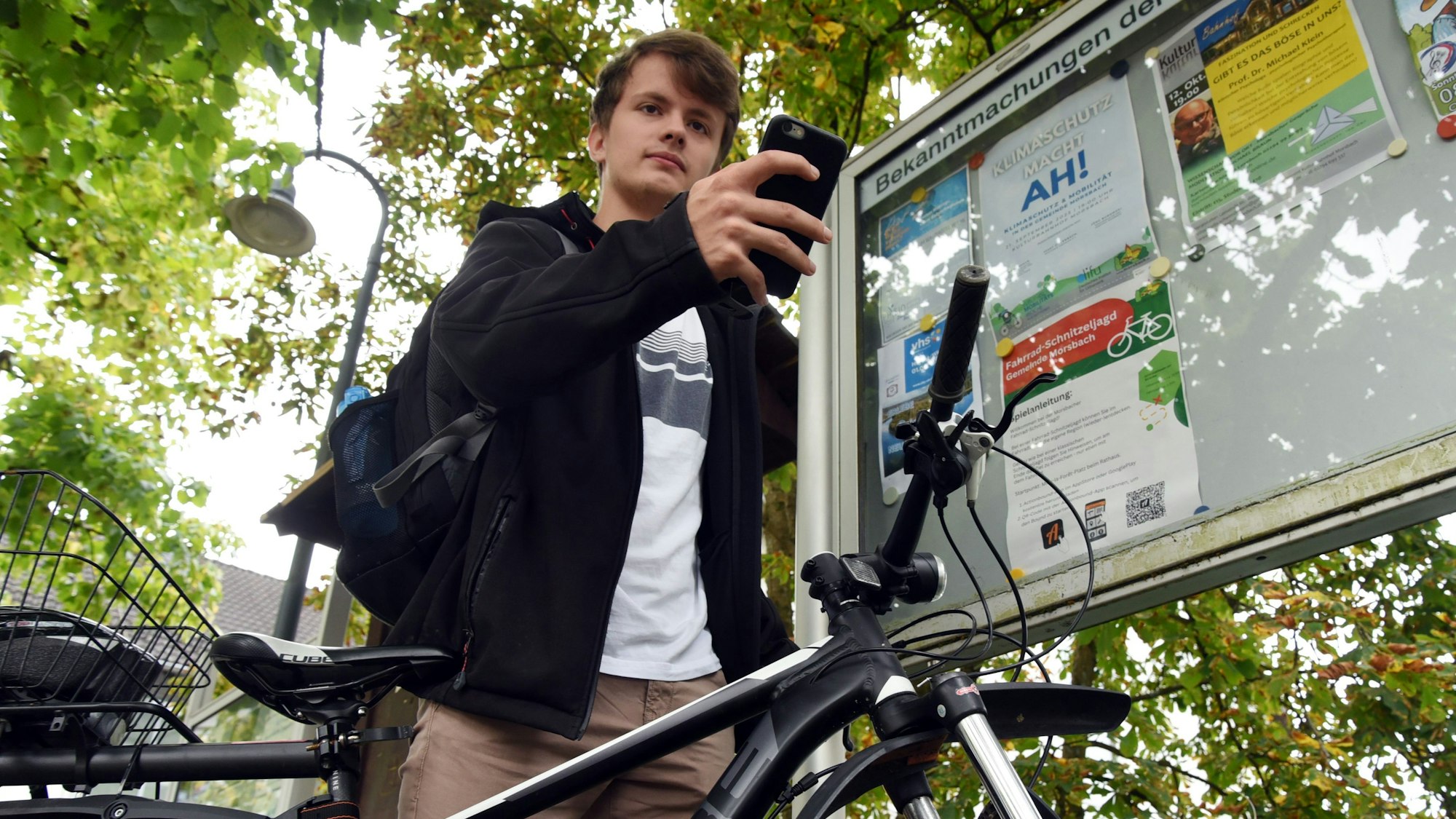 Robin Klein steht an seinem Fahrrad und hält ein Handy in der Hand.