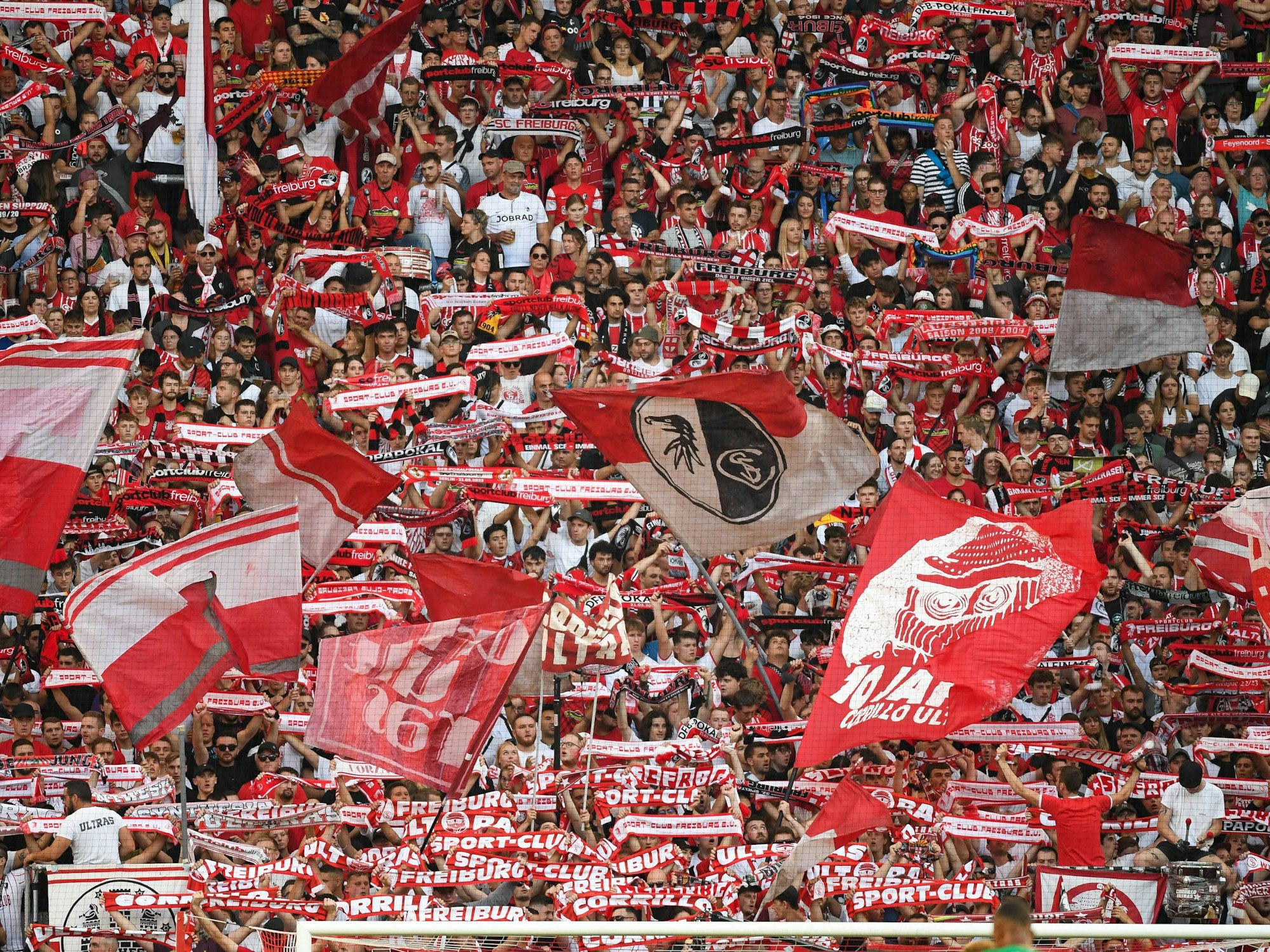 Die aktive Fanszene des SC Freiburg schwenkt Fahnen und streckt Schals in die Höhe.