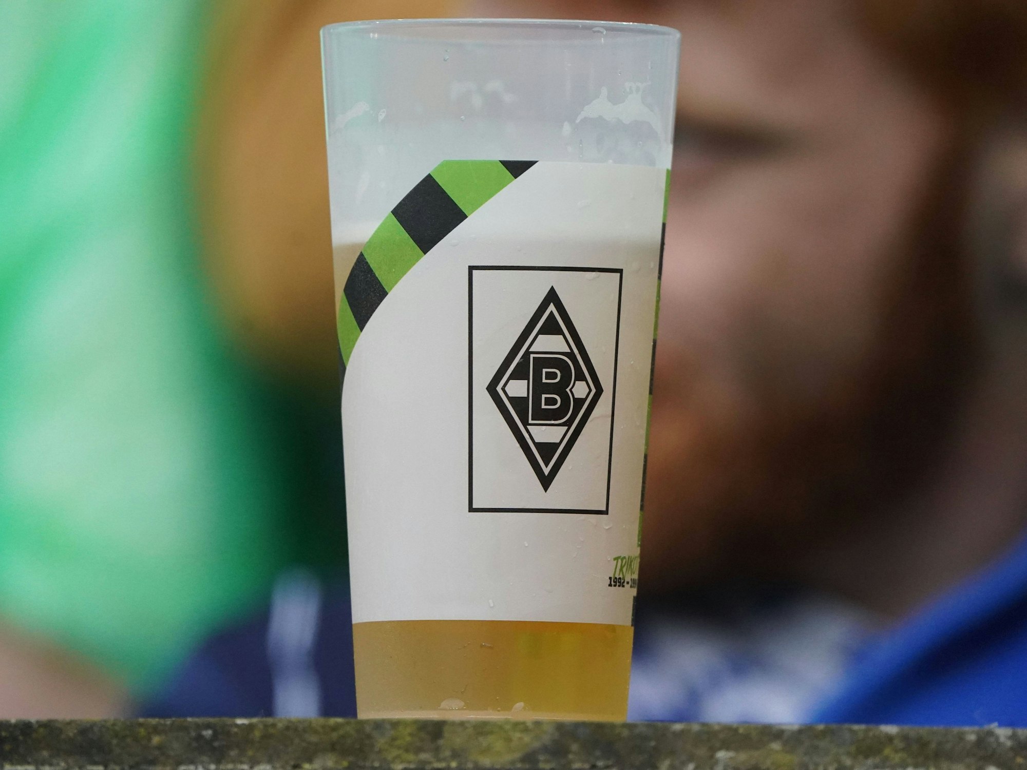 Ein halbvoller Bierbecher mit Borussia Mönchengladbach Logo steht vor einem Fan.