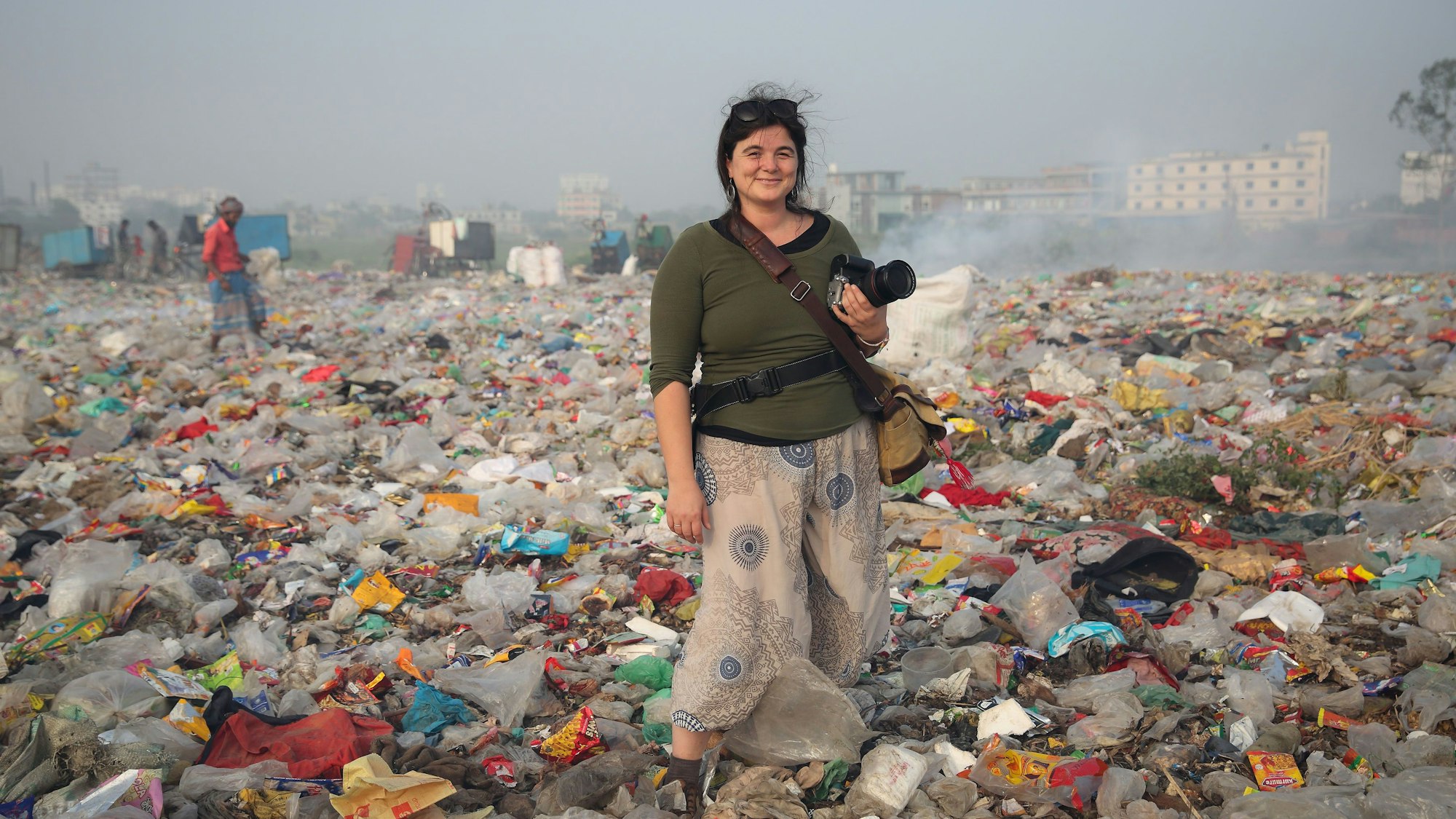 Alena Horst steht mit Kamera in der Hand in einer Müll-Landschaft.