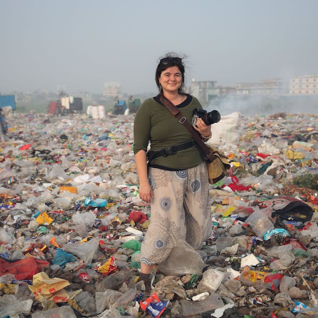 Alena Horst steht mit Kamera in der Hand in einer Müll-Landschaft.&nbsp;