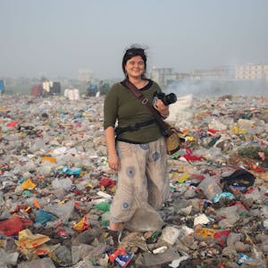 Alena Horst steht mit Kamera in der Hand in einer Müll-Landschaft.&nbsp;