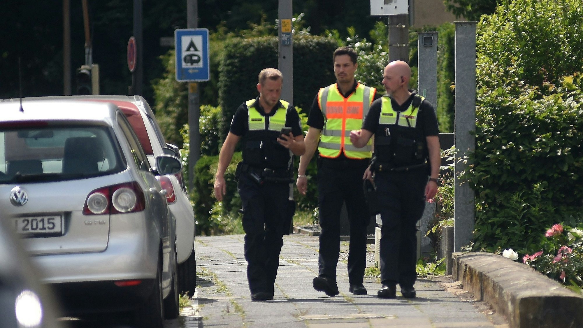 Drei männliche Mitarbeiter des Ordnungsdienst gehen an einer Straße entlang und informieren die Anwohner über eine Evakuierung.