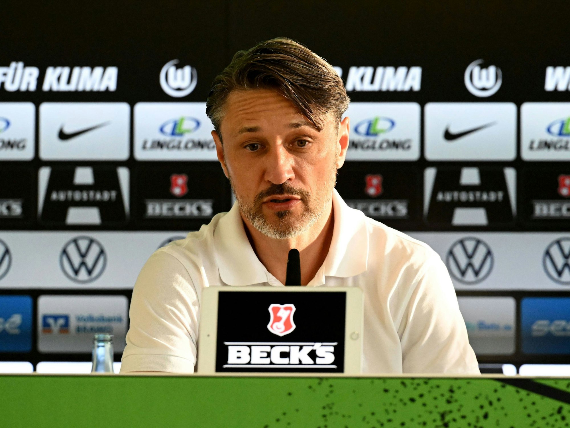 Niko Kovac sitzt bei einer Pressekonferenz hinter einem Mikrofon und einer elektronischen Anzeige, die das Logo Beck's zeigt.