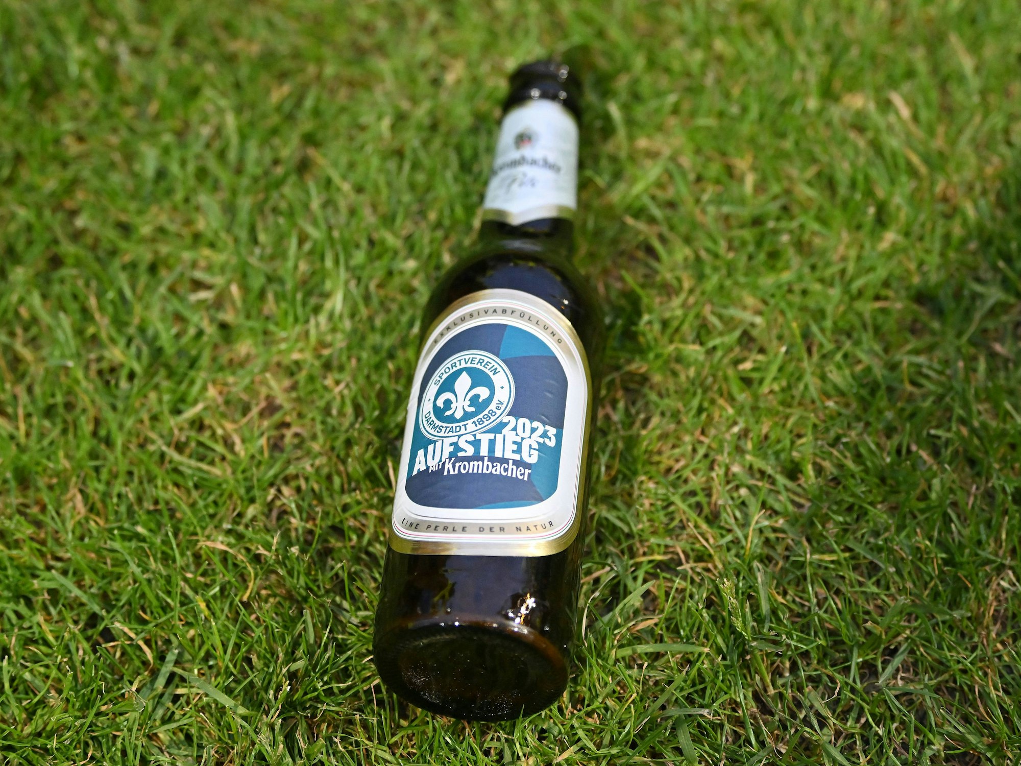 Eine Flasche Krombacher liegt auf dem Rasen. Es ist eine Sonderedition zum Aufstieg von Darmstadt 98 in die 1. Bundesliga.