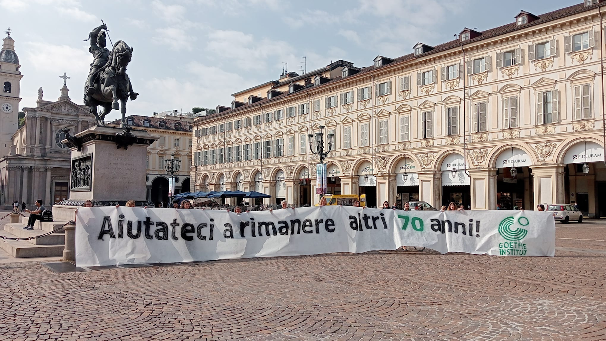 Das Bild zeigt den zentralen Platz in Turin San Carlo. Hier haben Mitarbeiter des Goethe-Instituts ein Banner aufgespannt, wo drauf steht: „Helft uns, weitere 70 Jahre zu bleiben“