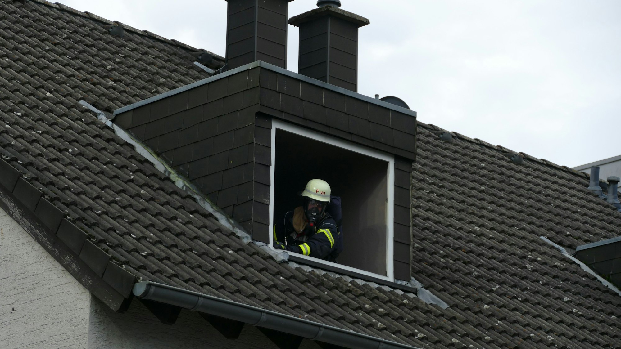 Ein Feuerwehrmann mit Atemschutz schaut aus einem Dachfenster.