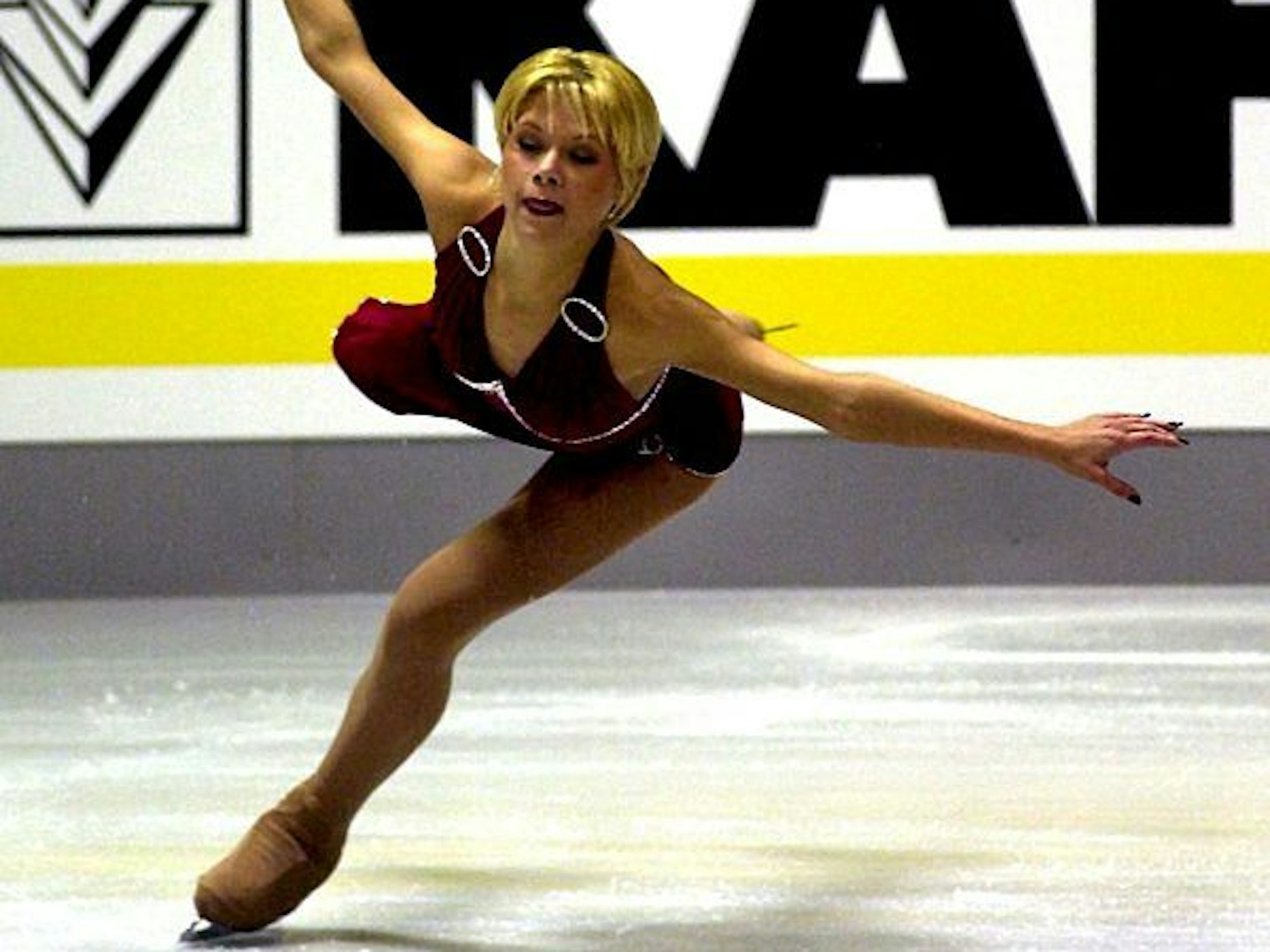 Eine junge blonde Eisläuferin gleitet im roten Kleid über das Eis. 