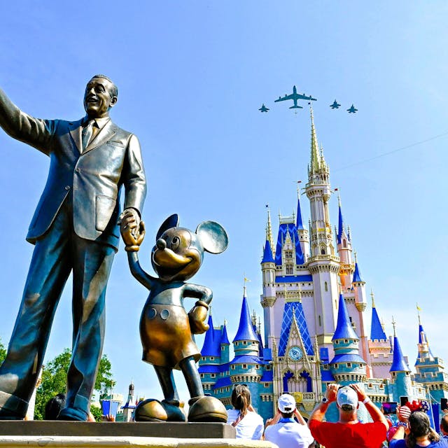 Die Staturen von Walt Disney und Mickey Mouse in der Disney World. Im Hintergrund überfliegen Flugzeuge das Cinderella Schloss.