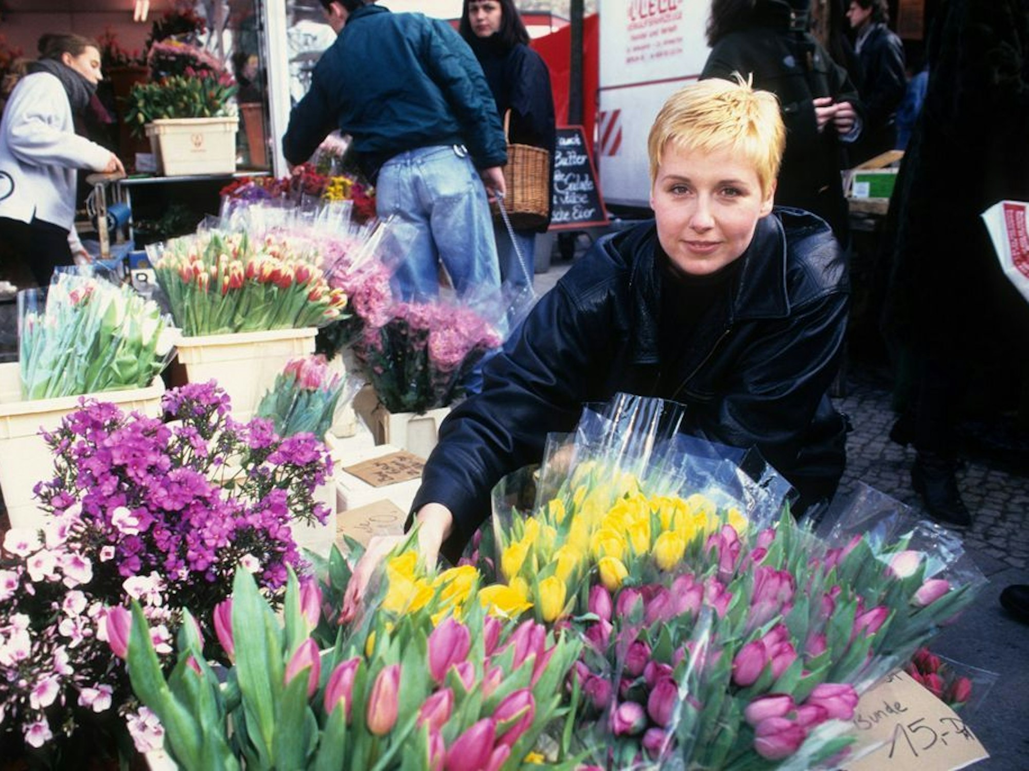 Eine junge Frau mit kurzen blonden Haaren und Lederjacke kauft Tulpen in einem Blumenladen.