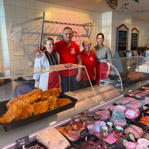 Das Foto zeigt eine Metzgerei mit einer Fleisch- und Wursttheke und vier Personen