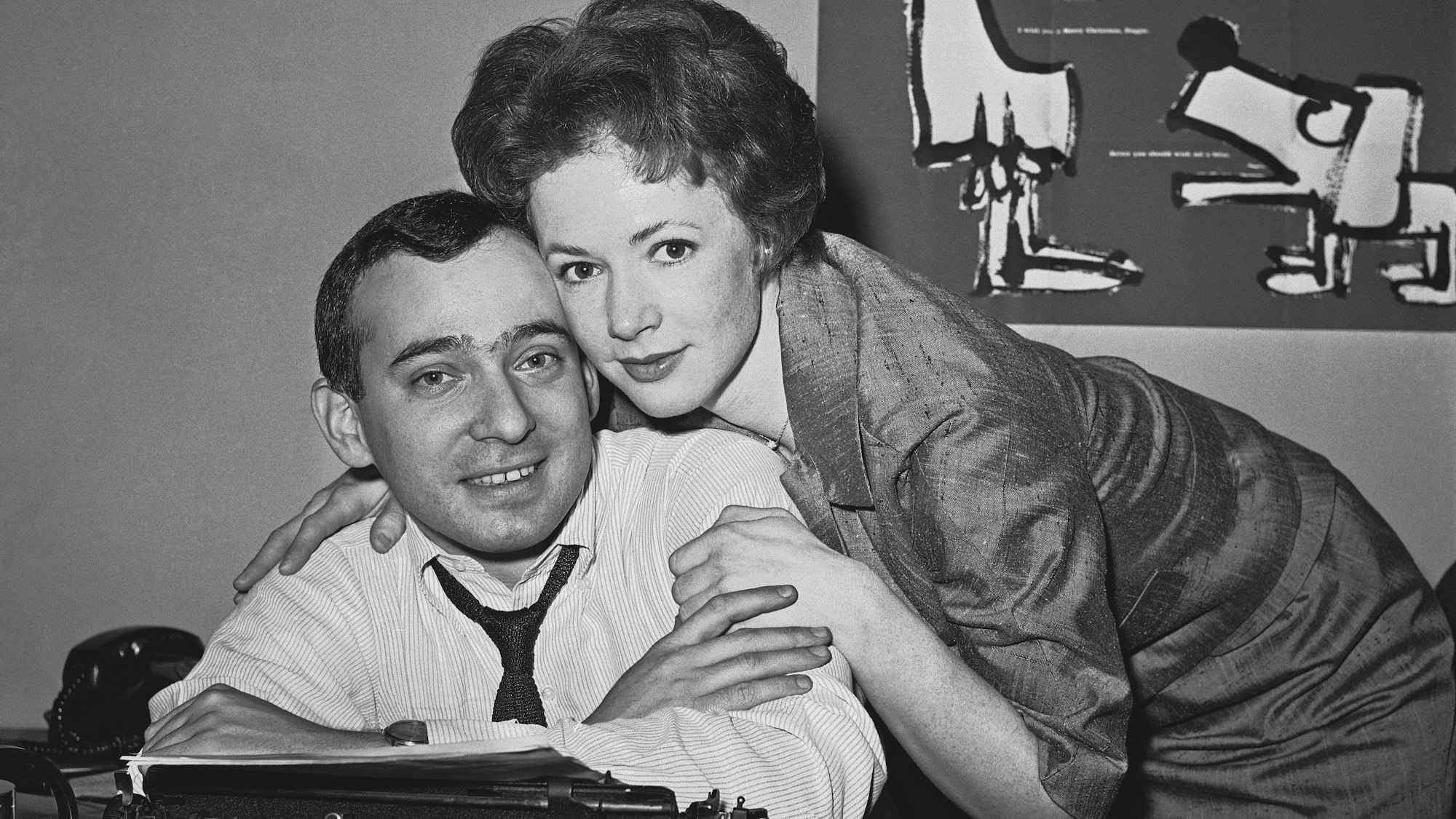 Die Schauspielerin Piper Laurie umarmt ihren zukünftigen Ehemann, den Theaterreporter und Kritiker Joseph M. Morgenstern, an seinem Schreibtisch bei der New Yorker „Herald-Tribune“, kurz nachdem ihre Eltern am 28. Dezember 1961 ihre Verlobung bekannt gegeben haben.
