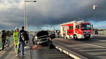 Ein verunfalltes Auto ist auf dem  Radstreifen auf der Kölner Zoobrücke gelandet. Im Hintergrund steht ein Feuerwehrauto auf der Fahrbahn.