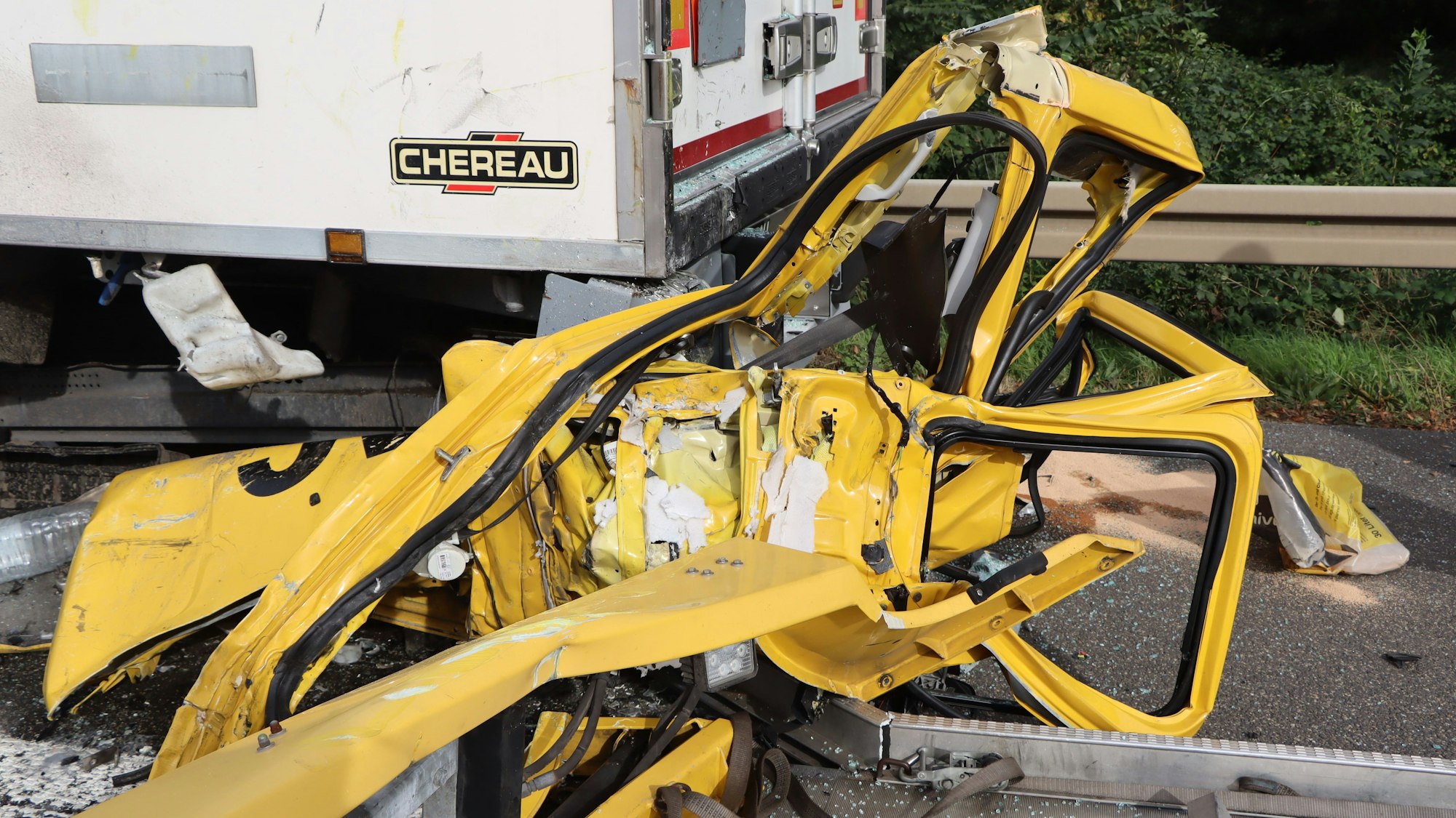 Der gelbe Kleinlastwagen eines Pannendienstes liegt völlig zerstört eingeklemmt unter einem Lkw am Standstreifen der Autobahn 553.