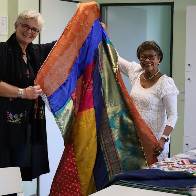 Zwei Frauen der Hennefer Patchwork-Gruppe halten einen Vorhang aus farbigen alten Saris hoch.