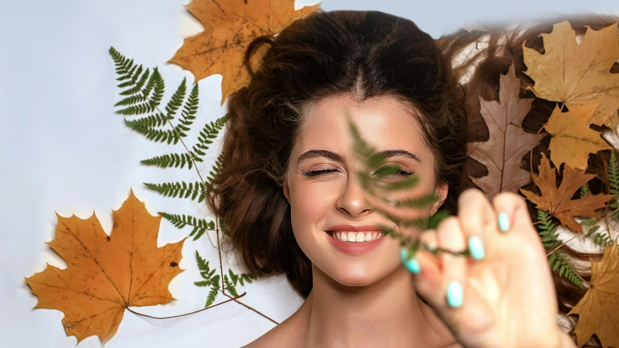 Eine junge Frau in herbstlicher Umgebung mit Blättern und Make-up in warmen, gedeckten Herbsttönen.