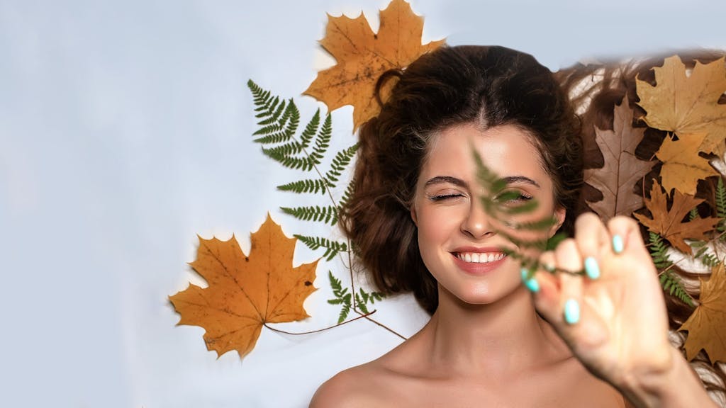 Eine junge Frau in herbstlicher Umgebung mit Blättern und Make-up in warmen, gedeckten Herbsttönen.