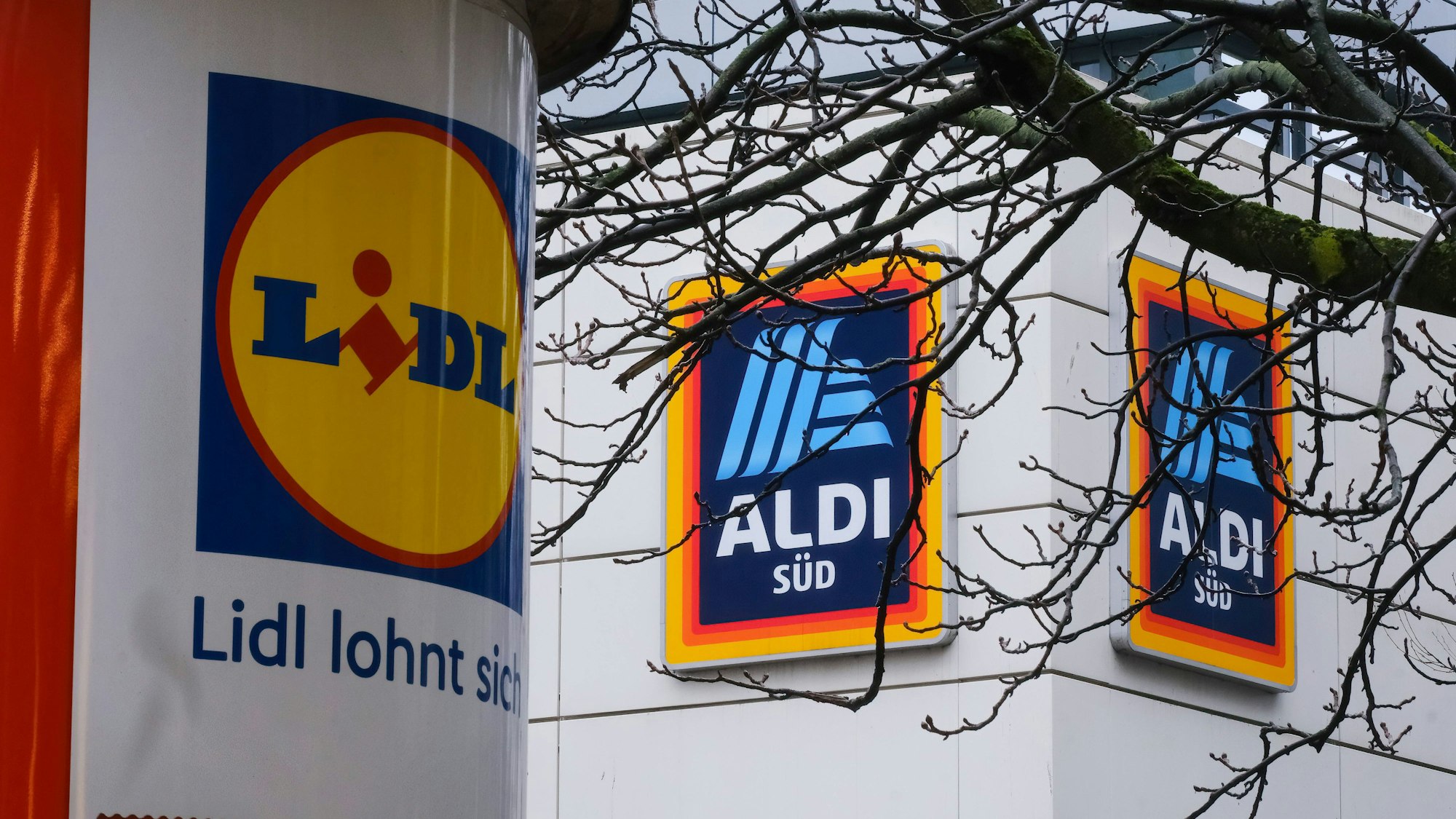 Eine mit einem Lidl-Logo beklebte Säule steht in Düsseldorf vor einer Aldi-Süd-Filiale.